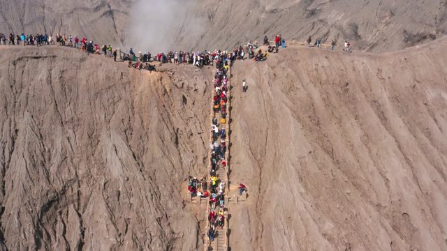 EAST JAVA, Indonesia - July 30, 2019: Aerial view of crowded tourists climbing stairs and enjoying Mount Bromo crater landscape. Shot in 4k resolution from a drone flying forwards