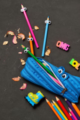 Funny Back to School concept - pencil case eating pencils on black chalk background. Space for text.