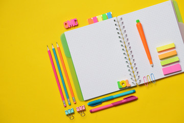 Colorful Back to School concept - open copy book with office and student supplies on yellow chalk. Space for text.