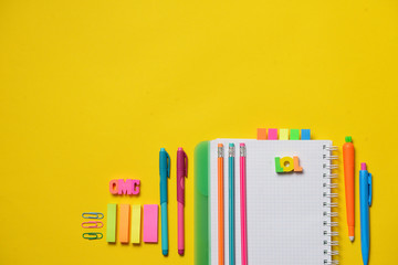 Colorful Back to School concept - open copy book with office and student supplies on yellow chalk. Space for text.