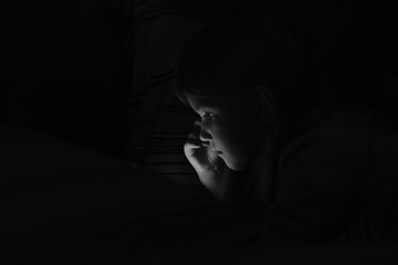 Young girl is watching something on a smart phone in a dark room with no lights
