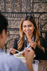 Portrait of two diverse Asian colleagues having a business lunch together. A tanned and attractive young Malay Asian woman is enjoying her salad as she talks to her Korean companion over lunch.