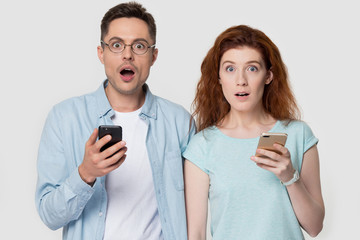 Shocked couple holds cell phones looking at camera pose indoors