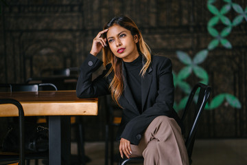 A portrait of a beautiful, young and attractive Asian woman manager, professional or entrepreneur in a pant suit sitting in a coworking space office during the day. She smiling confidently.