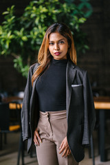 Portrait of a fashionable, capable and confident Southeast Asian woman in the city during the day. She is young, attractive and wearing a black turtleneck, khakis and has a jacket over her shoulders.