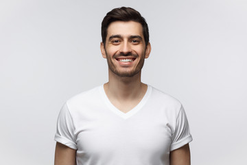 Smiling handsome young man in white t-shirt, looking at camera, isolated on gray background