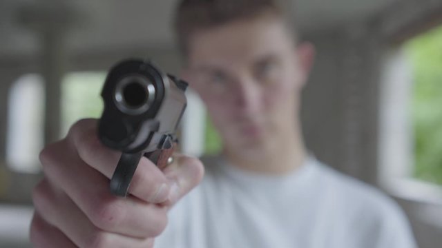 Young defocused man aiming with the pistol, his hands shaking close-up. The guy is going to kill the human in an abandoned building