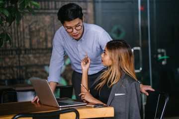 Candid shot of two young Asian businesspeople having a consultation for a business advice while sitting in a trendy coworking space during the day in the cafeteria. 