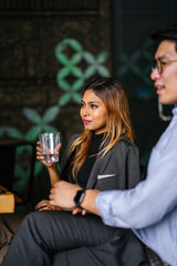 Portrait of a beautiful, fashionable, millennial Asian Malay businesswoman smiling to her colleague whose out of view and is sitting in a cafeteria while holding her cup of beverage during the day.