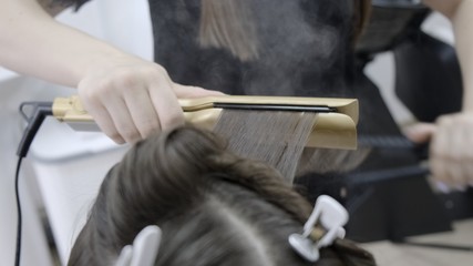 hairdresser makes hair lamination in a beauty salon for a girl with brunette hair. Close up