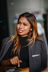 Fototapeta premium Portrait of a beautiful, fashionable, millennial Asian Malay businesswoman smiling to her colleague whose out of view and is sitting in a cafeteria during the day.