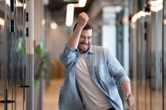 Ecstatic male winner dancing in office hallway laughing celebrating success