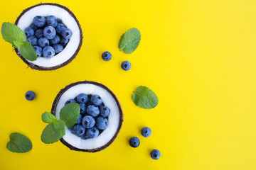 Blueberries  in half coconut on the yellow  background.Top view. Copy space.