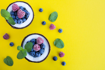 Blueberries and raspberries in the half coconut on the yellow  background.Top view. Copy space.