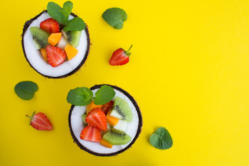 Fruit  salad in the  half coconut on the  yellow  background. Top view.Copy space.