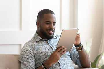 Smiling african man using digital tablet reading e-book at home