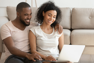 Happy african couple using laptop watching movie sit on floor