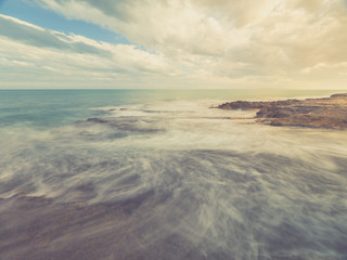 seascape at sunset with beach of rocks beaten by the sea and clouds moving in the sky