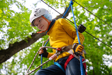 young boy in helmet in the rope park pass obstacles  route high among trees, extreme sport in adventure park