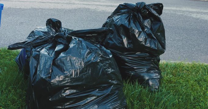 Black, plastic trash bags sitting on a curb waiting to be picked up by the garbage truck
