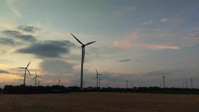 Wind turbines for green energy generation in fast motion time-lapse at dusk in Burgenland plains.