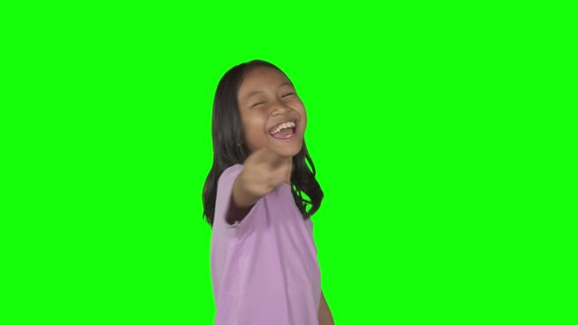 Little girl laughing and pointing at the camera looks bullying or mocking someone. Shot in 4k resolution with green screen background