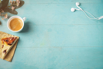 top view image of headphones, coffee cup and cheesecake on a wooden blue background, copy space