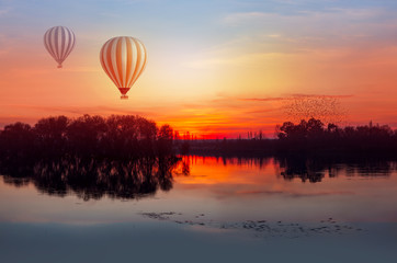 Birds silhouettes flying over the lake with two hot air balloons at sunset