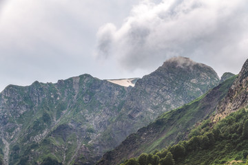 Clouds and fog on the slopes of mountain ranges with snowy peaks in summer.