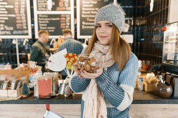 Winter portrait of young beautiful woman in knitted scarf, knitted hat, mittens, warm sweater with bowl of hazelnuts and walnuts.