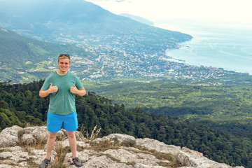 Naklejka premium Młody człowiek stojący na szczycie klifu w górach i podziwiając widok na przyrodę. Góry i morze