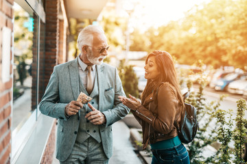 Senior father and his daughter using atm machine together to withdraw money. They are happy. Bright sunny day.