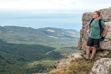 Obraz premium Young man with a backpack on top of cliff enjoying view of nature. Mountains and sea