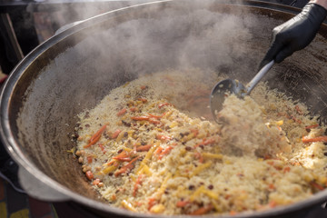 Cooking pilaf in a large cauldron on the street. Asian cuisine