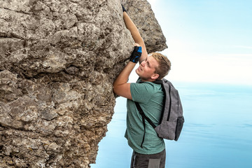 Young man hanging on edge, climbs up the rock