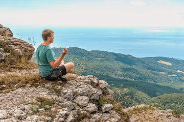 Young man practicing yoga pose sitting on the rocky peak. Man do meditation and enjoying view