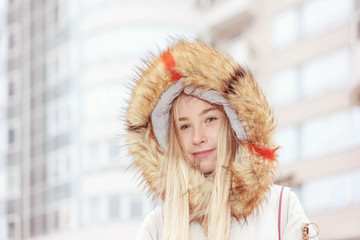 girl in a warm fur hood, urban glass buildings and houses with windows background
