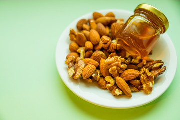 Nuts and honey in small jar, pot isolated on plate, on green background. Lunch in office. Detox, eating vegetarian. healthy eating concept. copy space