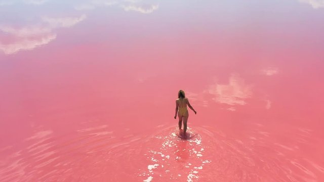 young woman going into the lake with bright pink water. Unique amazing landscape.