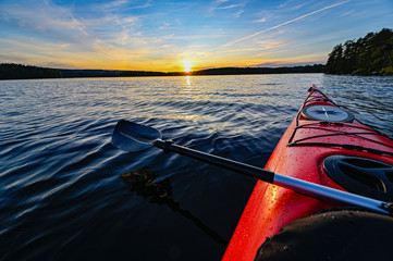red plastic kayak on calm water in the sunset - obrazy, fototapety, plakaty