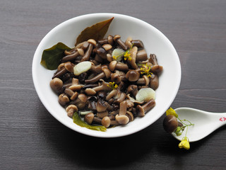Delicious and beautiful pickled mushrooms and spices in a white plate, one fungus in a spoon on a wooden background.  Home recipe pickles - small mushrooms with garlic and herbs close-up.