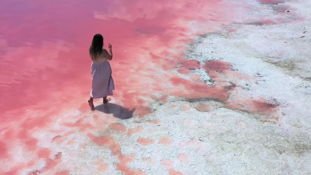 young woman walking and having fun near the unique lake with bright pink water color