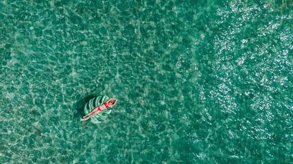 Summer lifestyle portrait of a beautiful girl swimming on her back on an inflatable palm leaf in the ocean.