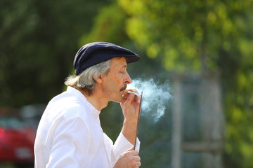 Mężczyzna odpala papierosa od metalowego pręta w parku. - obrazy, fototapety, plakaty