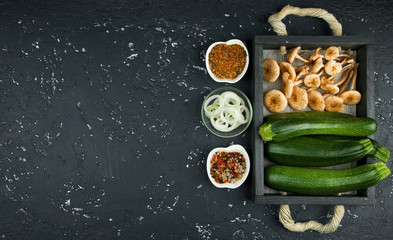 Fresh zucchini, mushrooms, spices and herbs on a black board. View from above. Copy space