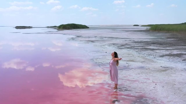 young woman walking and having fun near the unique lake with bright pink water color