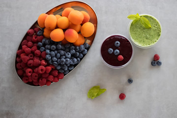 Fruit and berry smoothies and green smoothie. Fresh apricots, raspberries and blueberries on an oval metal plate. Gray background. Top view.