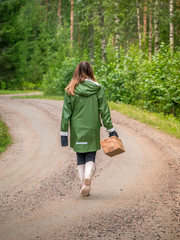 Girl with basket is picking chantarelles in the forest. Walking on dirt road seen from behind. © Adam