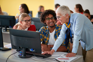 lecturer with group of students working in computer class on university campus.