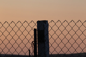 Wire fence close up with colored sky background; separation concept with hope for the future